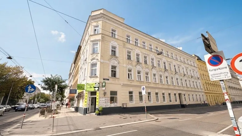 Historisches Eckgebäude in städtischer Umgebung mit klassischer Fassade und Geschäften im Erdgeschoss.