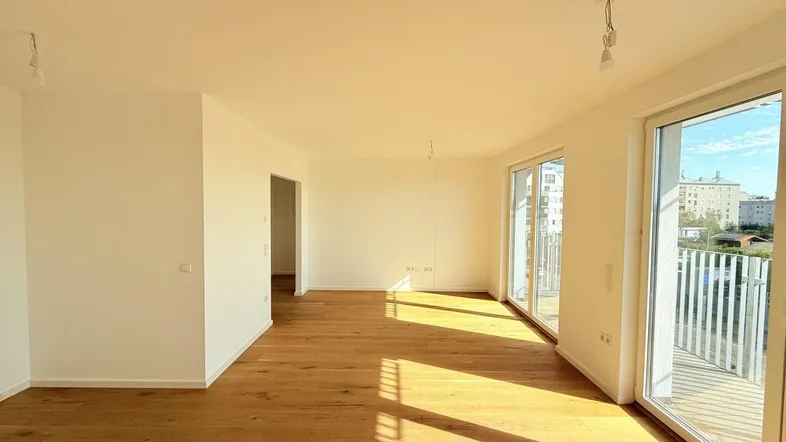Helles Wohnzimmer mit Eichenparkettboden, großen Fenstern und Zugang zu einem Balkon.