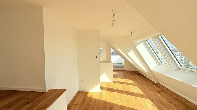 Helles Dachgeschosszimmer mit Holzboden, schrägen Wänden und großen Dachfenstern, die viel Licht hereinlassen.