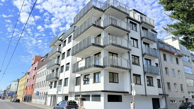 Modernes Wohngebäude mit vielen Balkonen und klarer Architektur unter blauem Himmel.