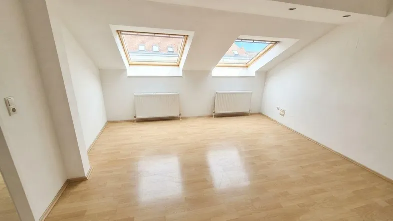 Helles Dachzimmer mit zwei Dachfenstern, Holzfußboden und Schrägen für viel Tageslicht.