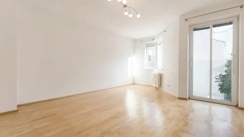 Helles Wohnzimmer mit Parkettboden, weißen Wänden und Zugang zu einem Außenbereich.