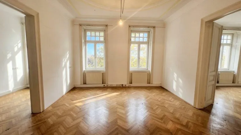 Helles Zimmer mit Fischgrätparkett und hohen Decken, durch zwei Fenster gut belichtet.
