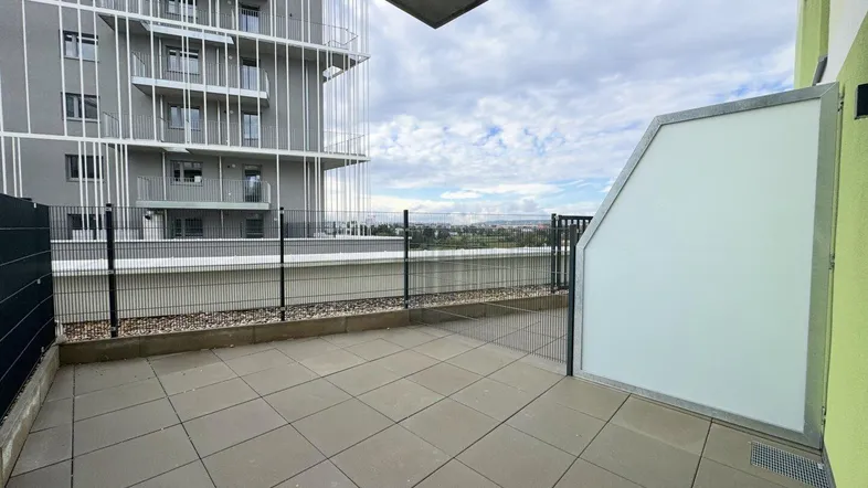 Geräumige Terrasse mit Fliesenboden und Blick auf die umliegende Landschaft und moderne Gebäude.