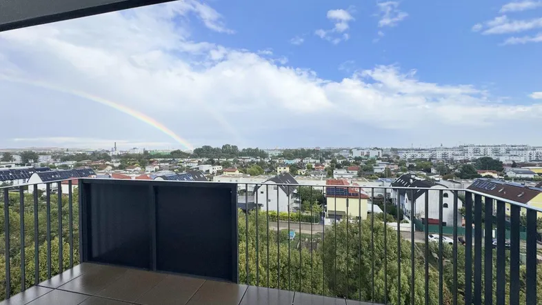 Balkon mit Stadtblick und einem Regenbogen am Himmel über der Vorstadtlandschaft.