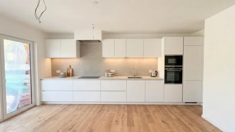 Moderne Einbauküche mit weißen Schränken, integrierten Geräten und hellem Holzboden.