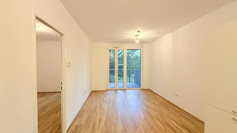 Helles Wohnzimmer mit Parkettboden, weißen Wänden und Zugang zu einem Balkon.