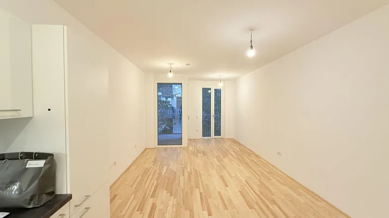 Heller Wohn- und Essbereich mit neuem Parkettboden und Zugang zu einem Balkon.