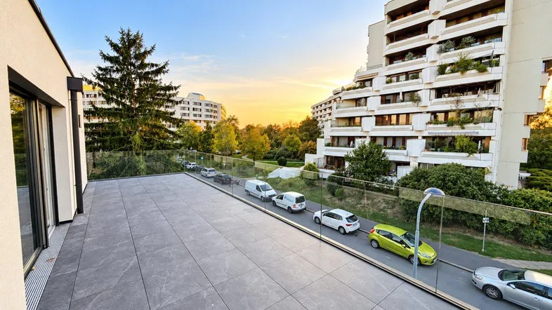 Große, modern geflieste Terrasse mit Glasgeländer und Blick auf die umliegenden Gebäude bei Sonnenuntergang.
