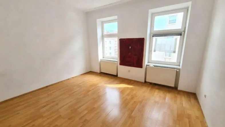 Helles Zimmer mit Parkettboden, weißen Wänden und zwei Fenstern, ideal als Wohn- oder Schlafzimmer.