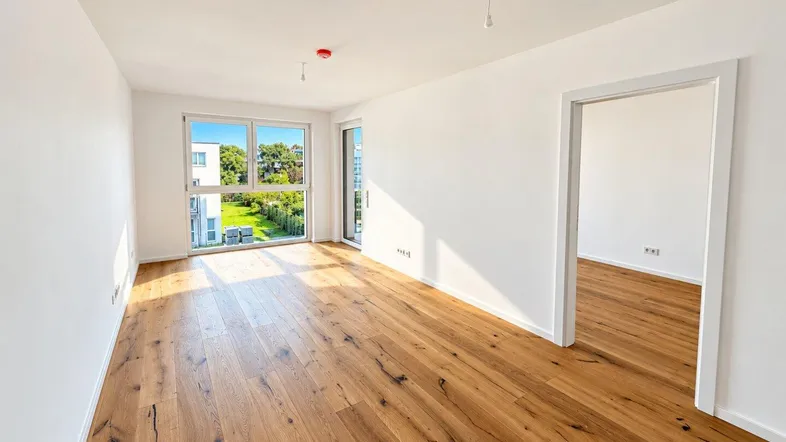 Heller Wohnraum mit hochwertigem Holzfußboden und Blick ins Grüne durch große Fenster.