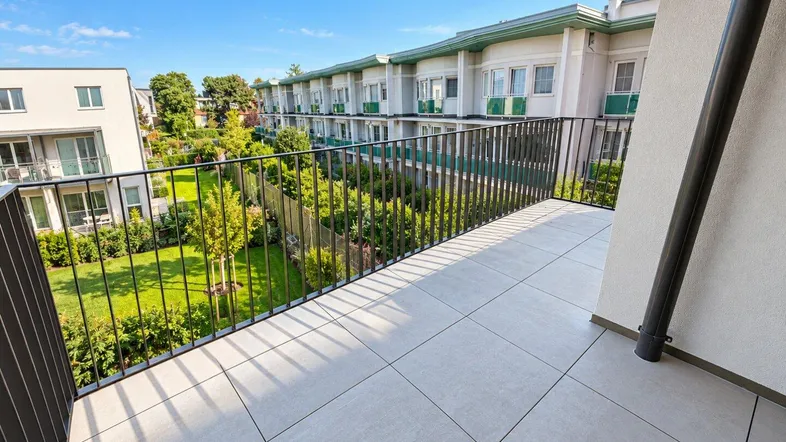 Geräumiger Balkon mit Fliesenboden und Blick auf den gepflegten Gemeinschaftsgarten und umliegende Gebäude.