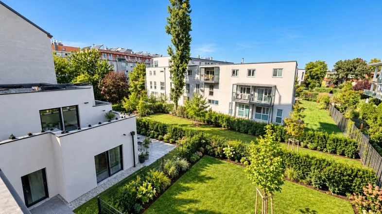 Luftaufnahme eines modernen Wohnkomplexes mit gepflegten Grünflächen und mehreren Gebäuden unter blauem Himmel.