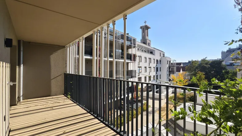 Geräumiger Balkon mit Holzboden und Blick auf die umliegenden Gebäude und einen Kirchturm.
