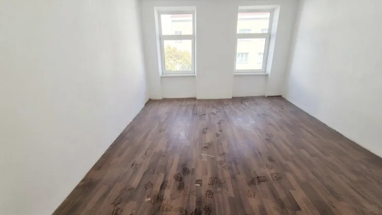 Leerer Raum mit dunklem Holzboden und zwei Fenstern, bereit für die individuelle Gestaltung.