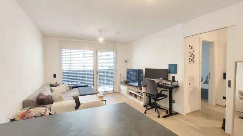 Helles Wohnzimmer mit Sofa, Arbeitsbereich und Zugang zu einem Balkon oder einer Loggia.