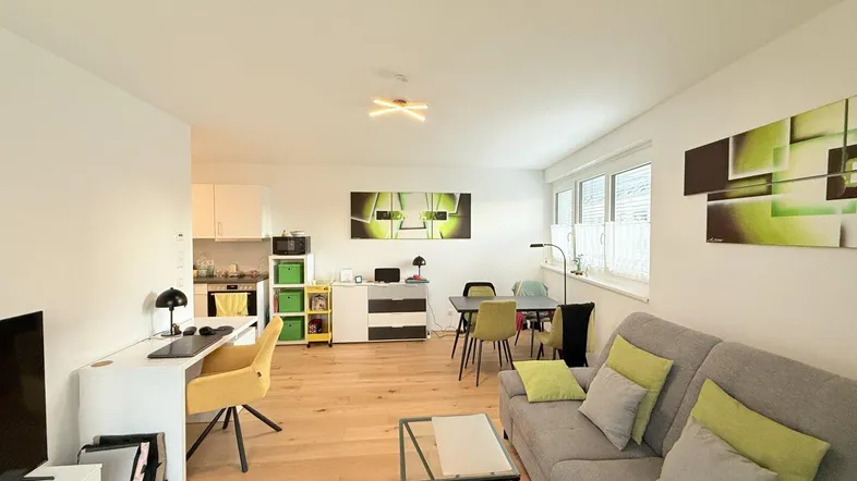 Helles, offenes Wohn-Esszimmer mit Holzboden, Schreibtisch und Zugang zur Küche.