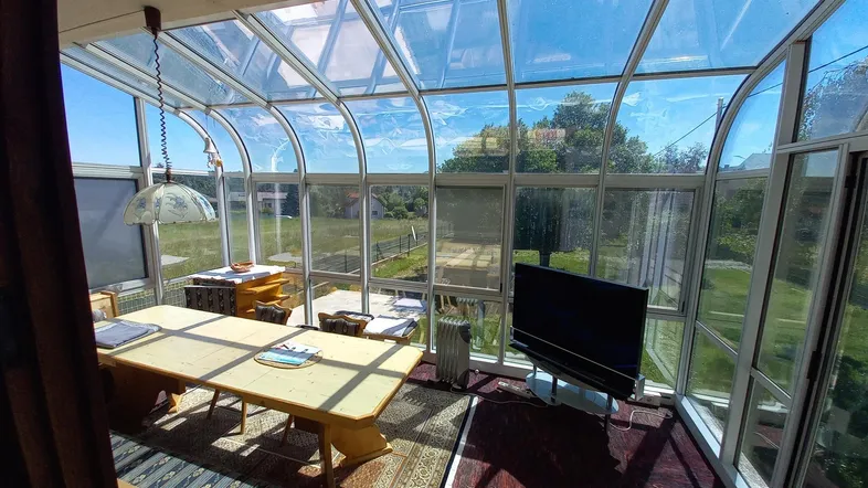 Heller Wintergarten mit Glasdach, Essbereich und weitem Blick ins Grüne.