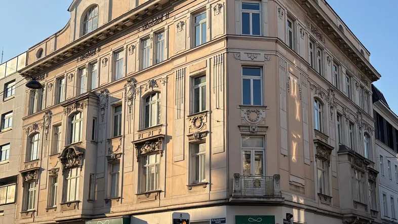 Historisches Eckgebäude mit reich verzierter Stuckfassade und Geschäften im Erdgeschoss.