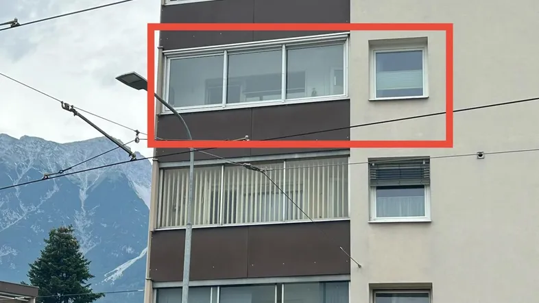 Mehrstöckiges Wohngebäude mit Balkonen und Fenstern, umgeben von Bergen und Bäumen.