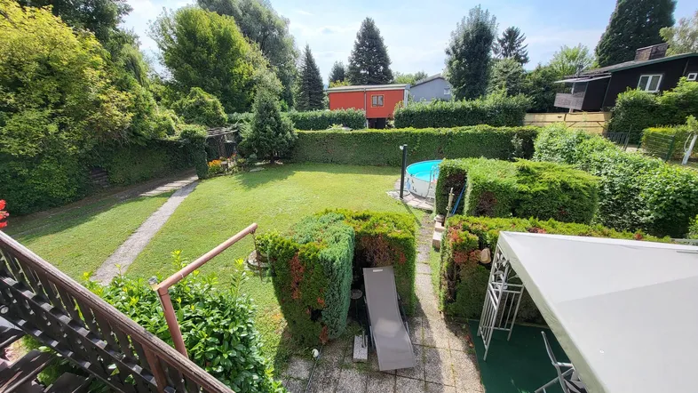Weitläufiger Blick von oben auf den gepflegten Garten mit Pool und üppiger Vegetation.