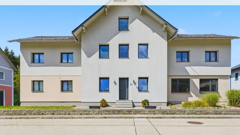 Frontansicht eines modernen Einfamilienhauses mit heller Fassade und mehreren Fenstern.