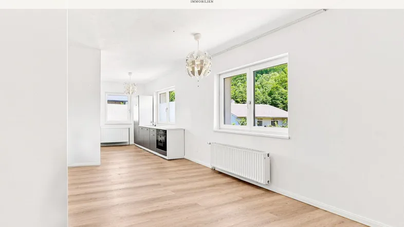 Heller offener Wohnbereich mit modernem Laminatboden, großen Fenstern und Blick ins Grüne.