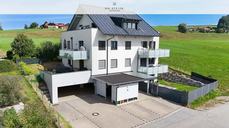 Modernes Mehrfamilienhaus mit mehreren Balkonen, Carport und Garten in ländlicher Umgebung.