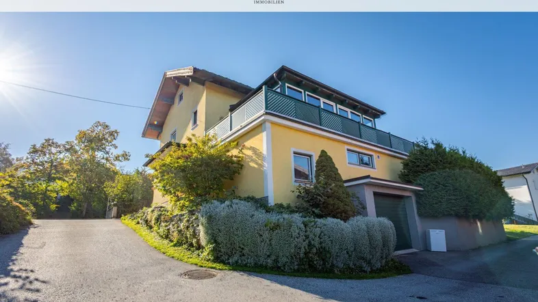 Gelbes Einfamilienhaus mit grünen Fensterrahmen und integrierter Garage unter strahlend blauem Himmel.