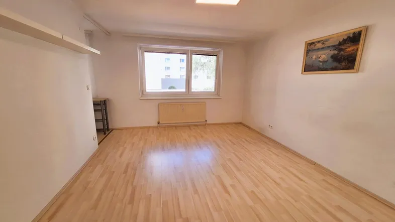 Helles Zimmer mit Parkettboden, weißen Wänden und einem Fenster, das Tageslicht hereinlässt.