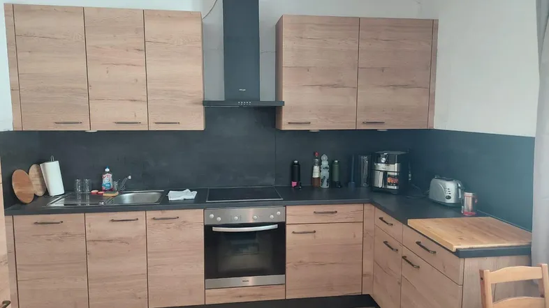 Moderne Küche mit Holzfronten, dunkler Arbeitsplatte und integrierten Geräten.