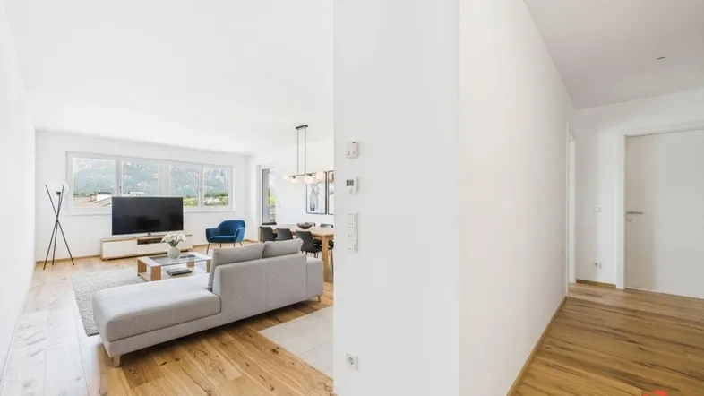 Helles, offen gestaltetes Wohn-Esszimmer mit Holzboden, modernen Möbeln und Bergblick.