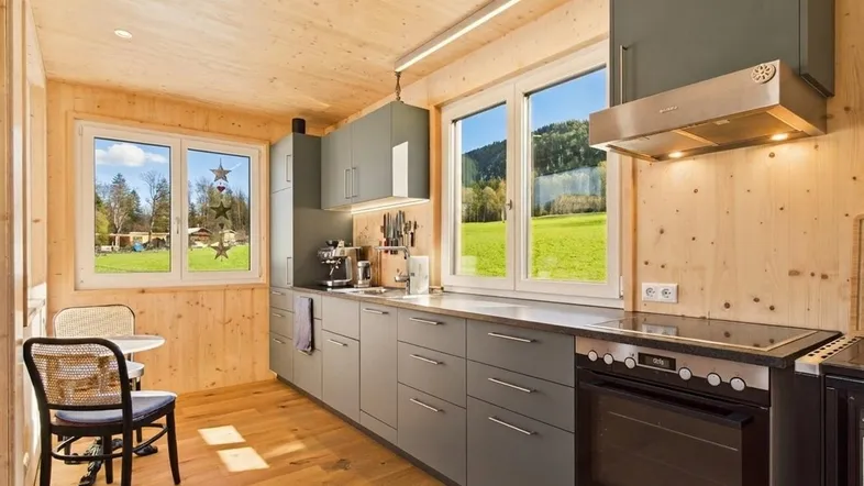 Moderne Küche mit Holzverkleidung, grauen Schränken und Blick ins Grüne.