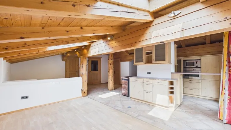 Helles, offenes Wohnzimmer mit Holzbalkendecke, Dachfenster und integrierter Küche.