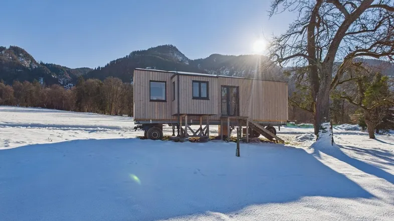 Modernes Tiny House aus Holz auf Rädern in einer verschneiten Landschaft mit Bergblick.
