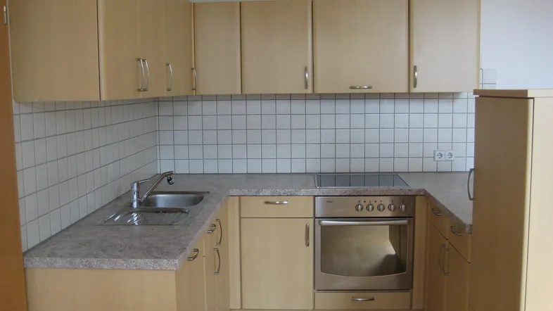 Helle Einbauküche mit hellbraunen Holzfronten, Granitarbeitsplatte und weißen Fliesen an der Wand.