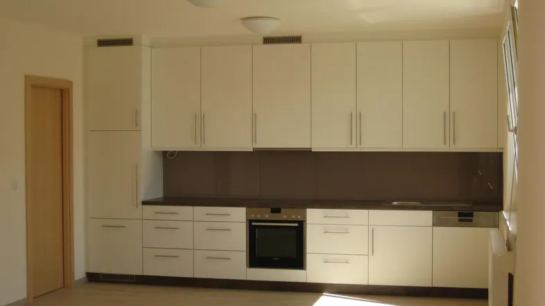 Moderne Einbauküche in Weiß mit dunkler Arbeitsplatte und Laminatboden, hell durch Tageslicht.