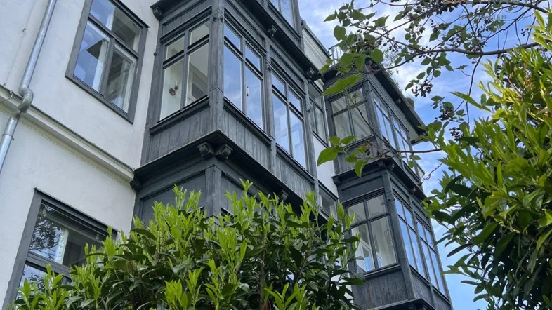 Fassade eines Gebäudes mit mehreren dunklen Erkern und grüner Bepflanzung unter blauem Himmel.