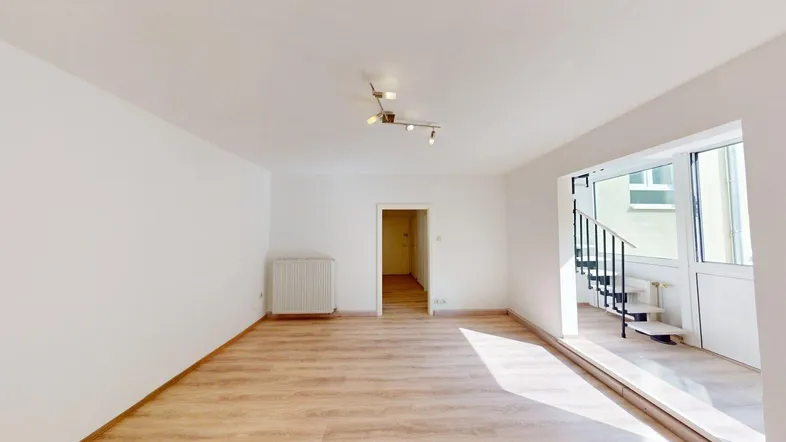 Helles Wohnzimmer mit Laminatboden, weiß gestrichenen Wänden und Zugang zu einem Balkon.