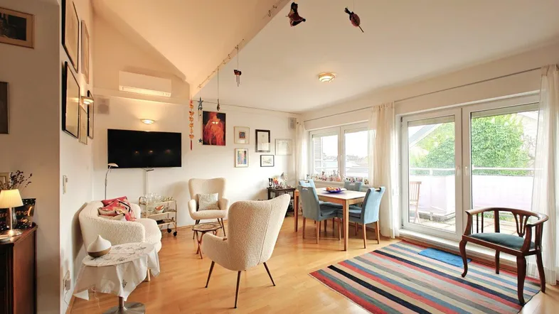 Helles Wohn- und Esszimmer mit Holzboden, Dachschräge und Zugang zum Balkon.