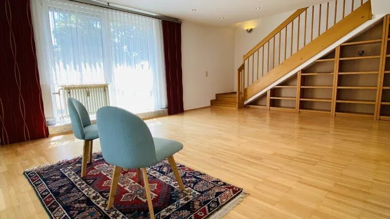 Helles Wohnzimmer mit Parkettboden, Einbauregalen und Treppe zum Obergeschoss.