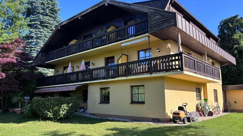 Großzügiges Haus mit mehreren Balkonen und gepflegtem Gartenbereich unter blauem Himmel.