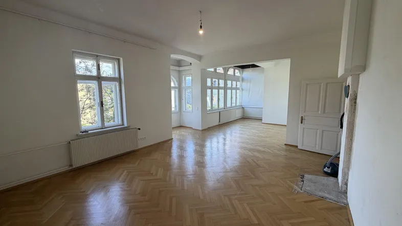 Helles Zimmer mit Fischgrätparkettboden und großen Fenstern, das viel Tageslicht hereinlässt.