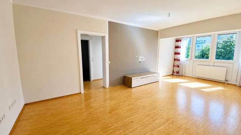 Helles Wohnzimmer mit Parkettboden, einer Akzentwand und großen Fenstern, die viel Tageslicht hereinlassen.