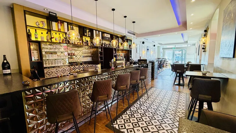 Eine moderne Bar mit stilvollen Hockern, einer gut bestückten Theke und dekorativen Hängelampen.