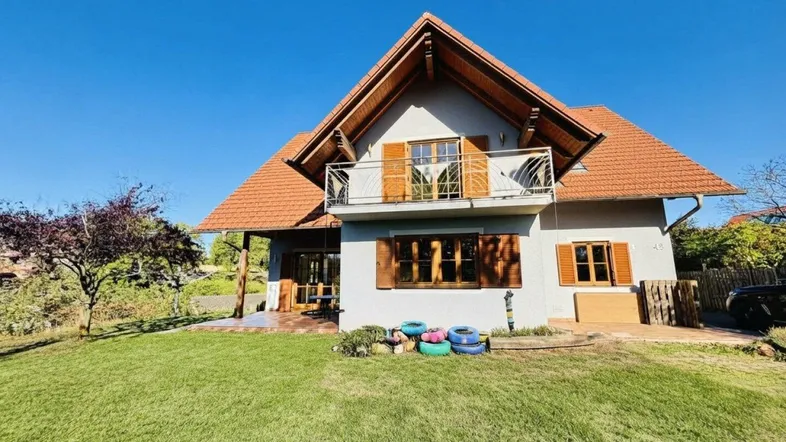 Freistehendes Haus mit Satteldach, Balkon und großem Garten an einem sonnigen Tag.
