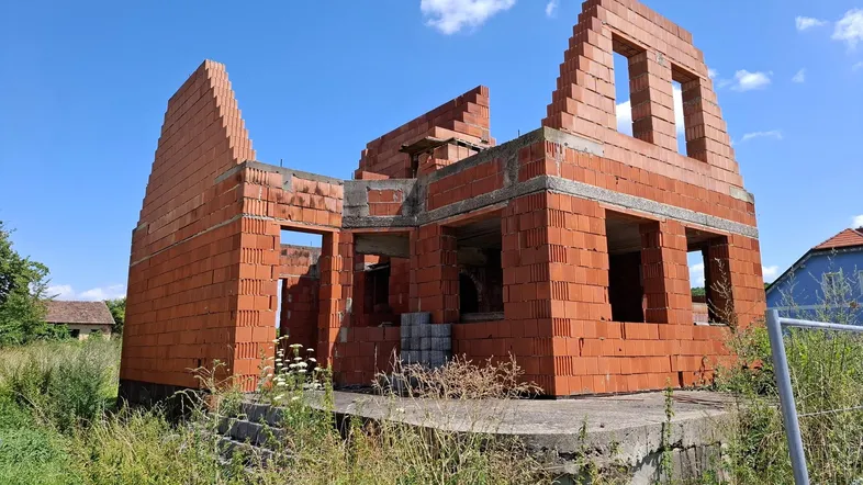 Rohbau eines Einfamilienhauses mit Ziegelmauerwerk und offener Bauweise unter blauem Himmel.