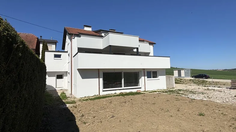 Modernes Wohnhaus mit weißer Fassade und großzügigen Balkonen, umgeben von einer noch unfertigen Gartenfläche.