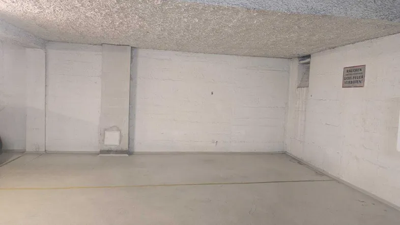 Leerer Parkplatz in einer Tiefgarage mit Betonwänden und -boden.