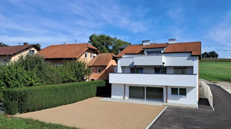 Modernes Neubauhaus mit weißer Fassade, Balkon und großem Grundstück in ländlicher Umgebung.